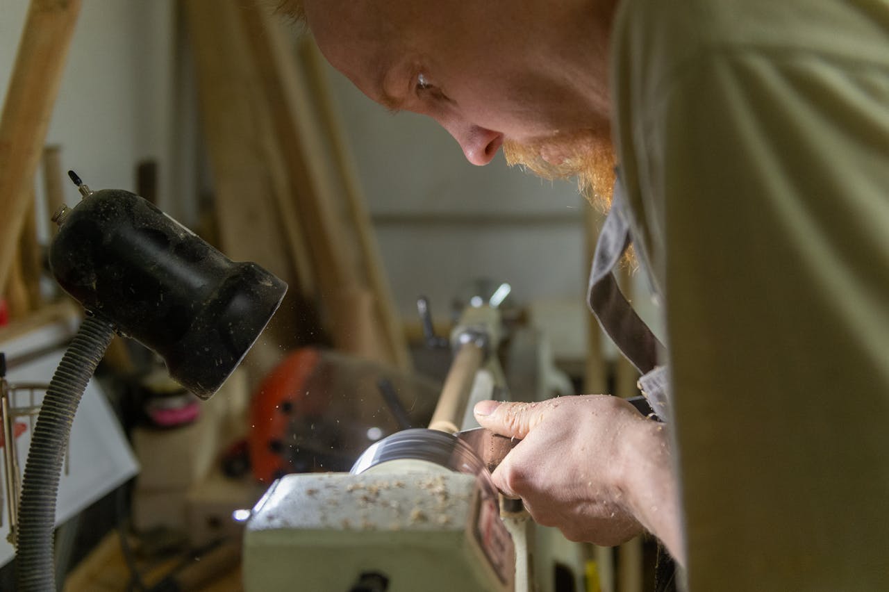 An artisan skillfully shapes wood on a lathe under focused workshop lighting.